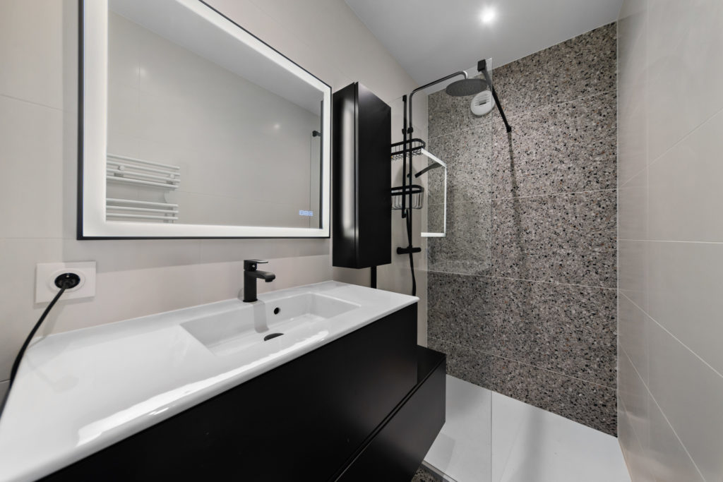 Salle de bain design avec douche à l'italienne, parois vitrées noires et faïence murale aspect marbre.